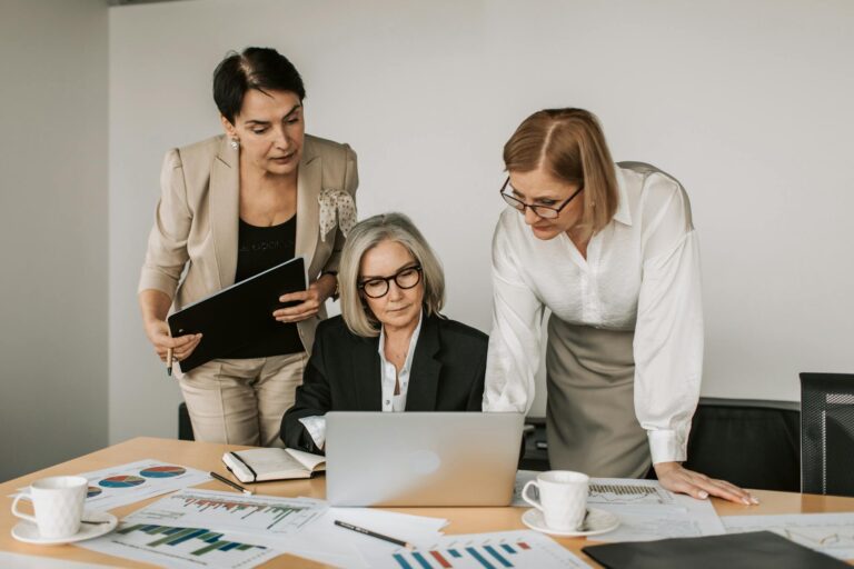 Three women in a business meeting, discussing strategy with charts and laptop.